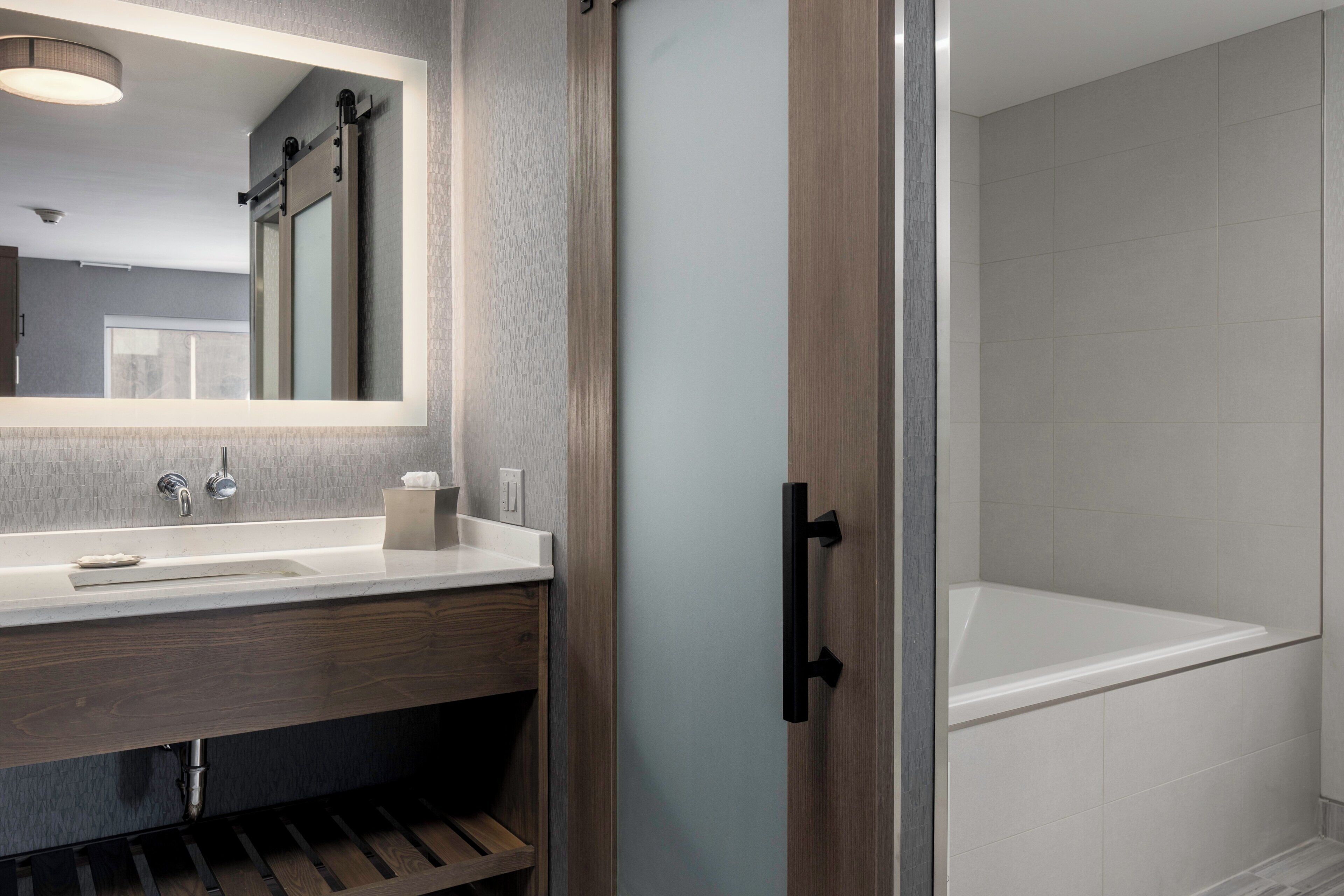 A modern bathroom with a large mirror, a sink, and a bathtub.