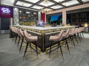 A modern bar area with a central island, bar stools, and a neon sign.