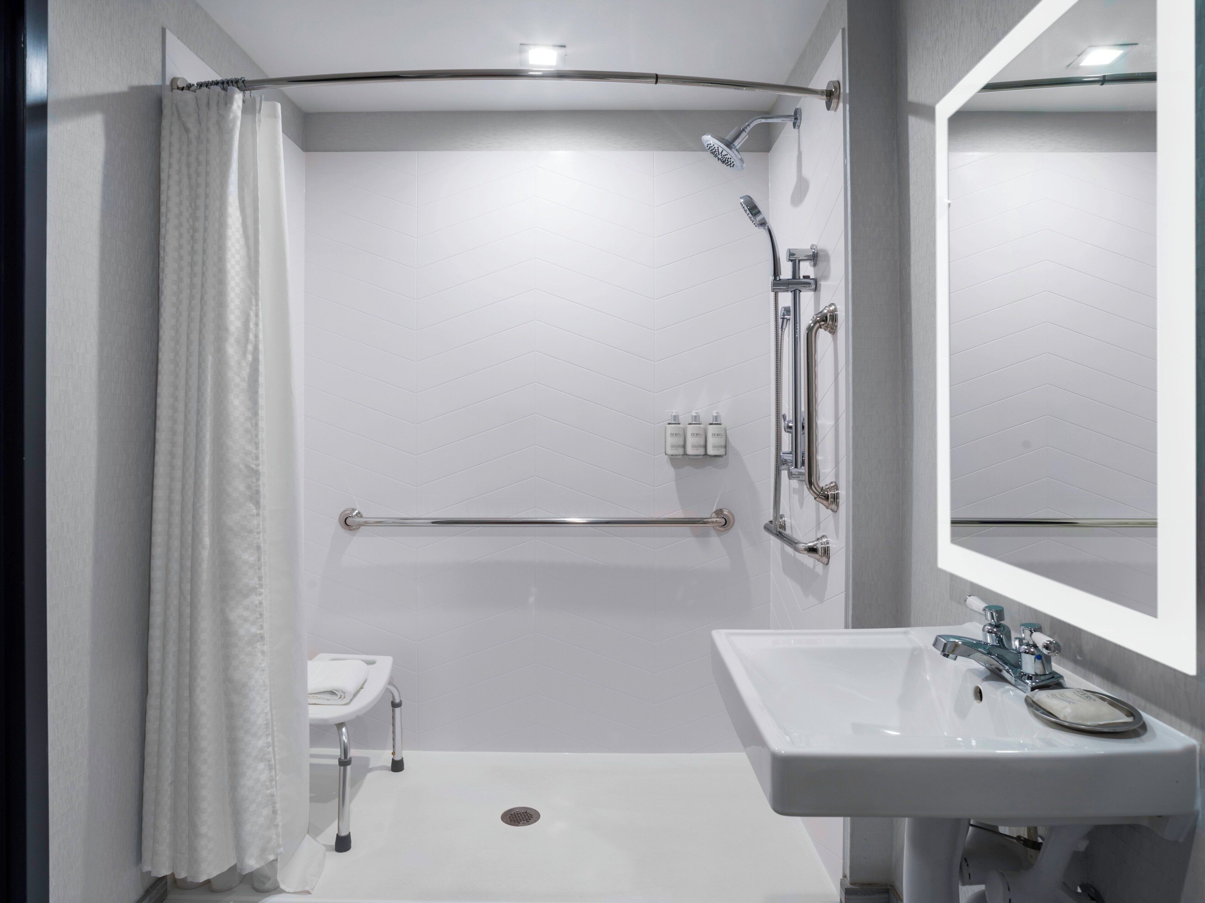 A modern bathroom with a shower, grab bar, and a sink with a mirror.