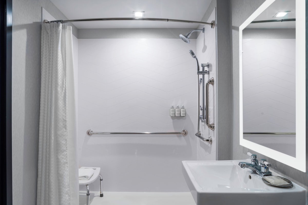 A modern bathroom with a shower, grab bar, and a sink with a mirror.