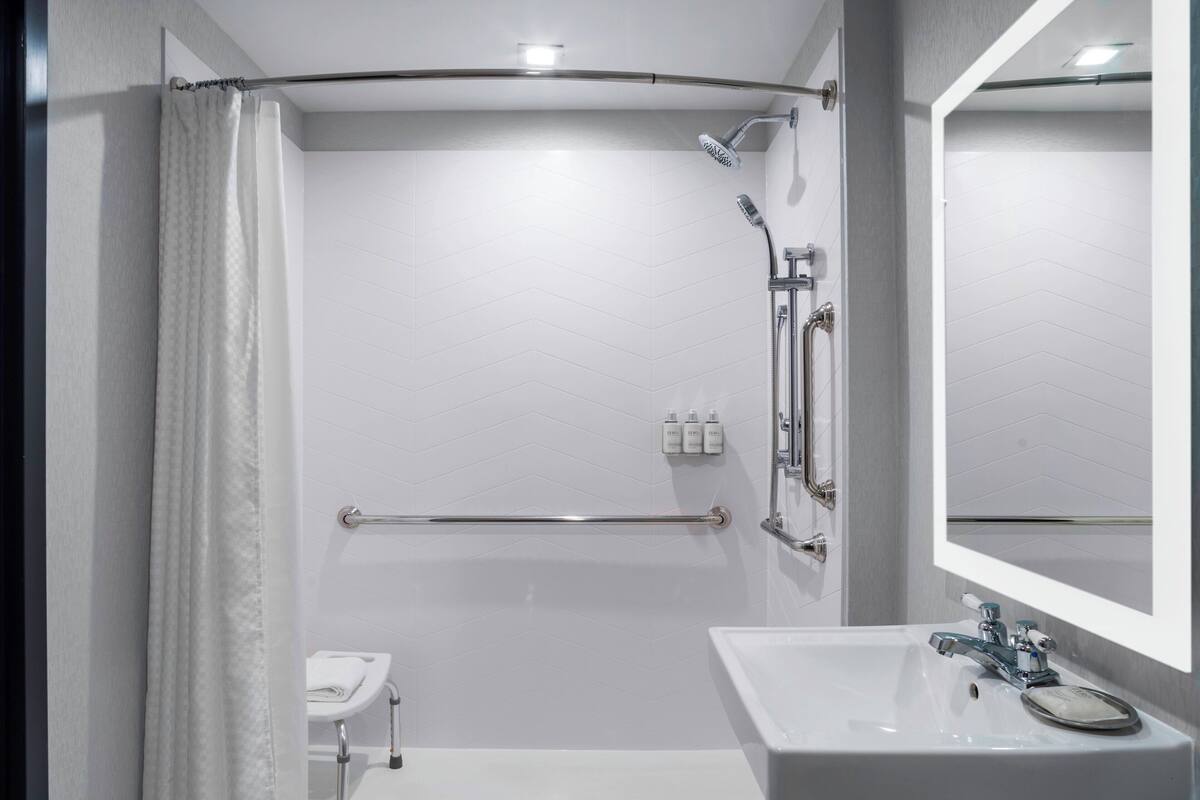 Un baño moderno con ducha, barra de apoyo y lavamanos con espejo.