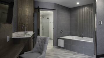 Un baño moderno con una bañera gris, un espejo grande y un sillón gris.