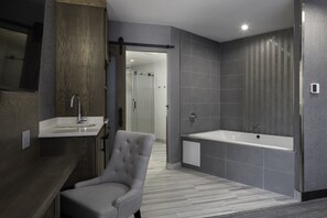 A modern bathroom with a grey bathtub, a large mirror, and a grey armchair.