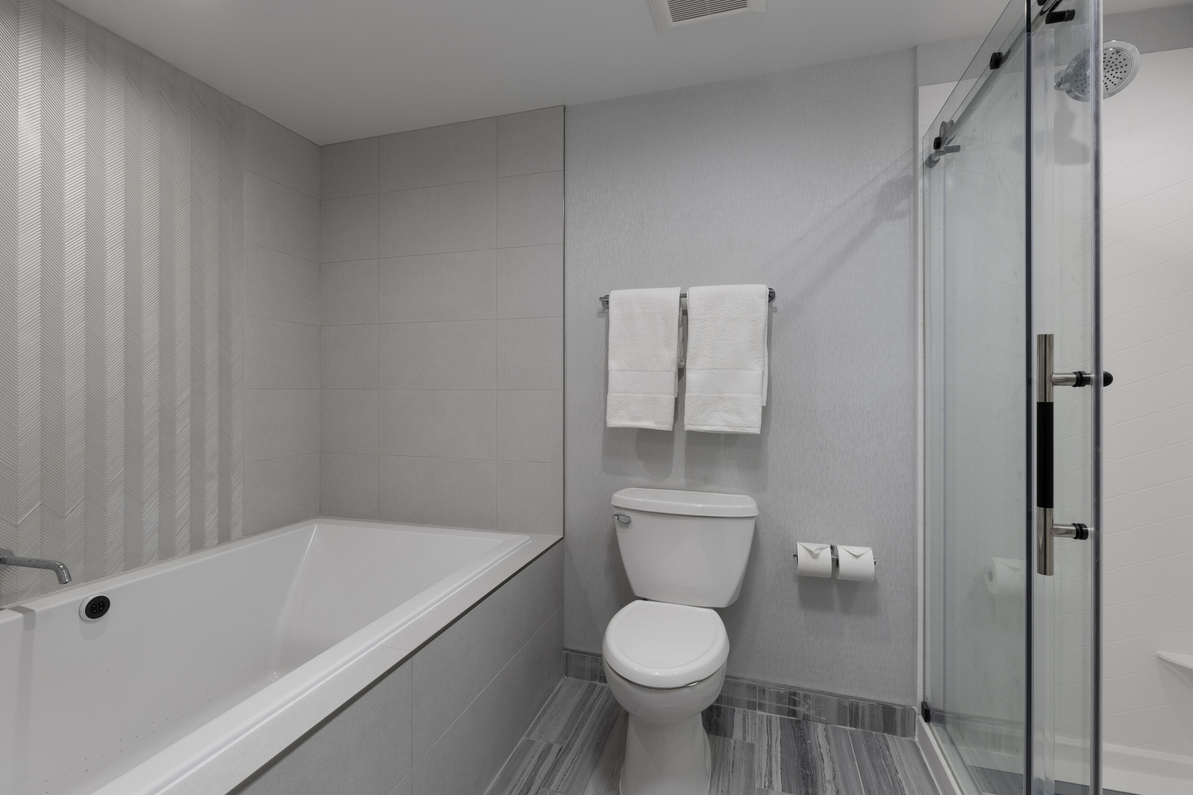 A modern bathroom with a bathtub, toilet, and glass shower enclosure.