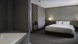 A modern hotel room with a large bathtub, a neatly made bed, and a wall-mounted towel rack.