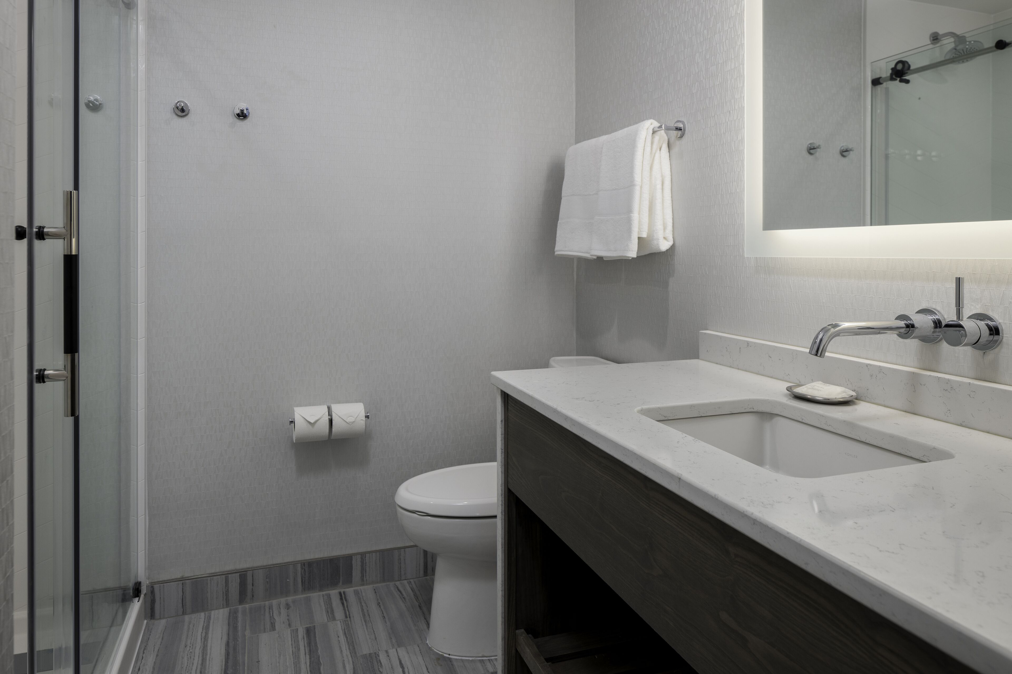 A modern bathroom with a glass shower enclosure, a white toilet, and a marble sink with a mirror above it.
