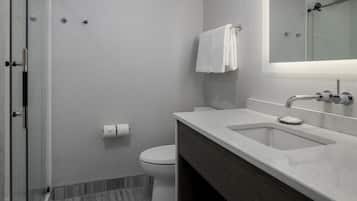 A modern bathroom with a glass shower enclosure, a white toilet, and a marble sink with a mirror above it.