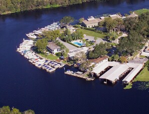An aerial view of a marina with multiple docked boats, a swimming pool, and several buildings. - Hontoon Landing Resort & Marina (DeLand)