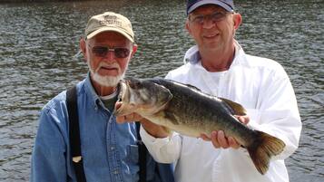 Two people holding a fish by a body of water.