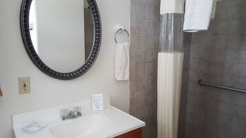 Un baño con un espejo redondo, un lavamanos, un perchero para toallas y una cortina de ducha.