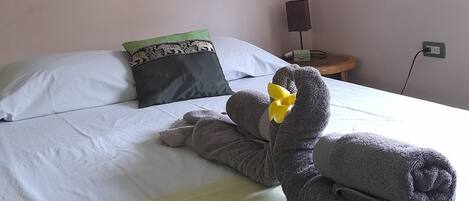 A hotel room with a bed, pillows, a teddy bear, and a wall-mounted air conditioner.
