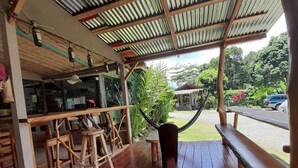 Una terraza de madera con techo de metal corrugado, taburetes de madera y una hamaca.