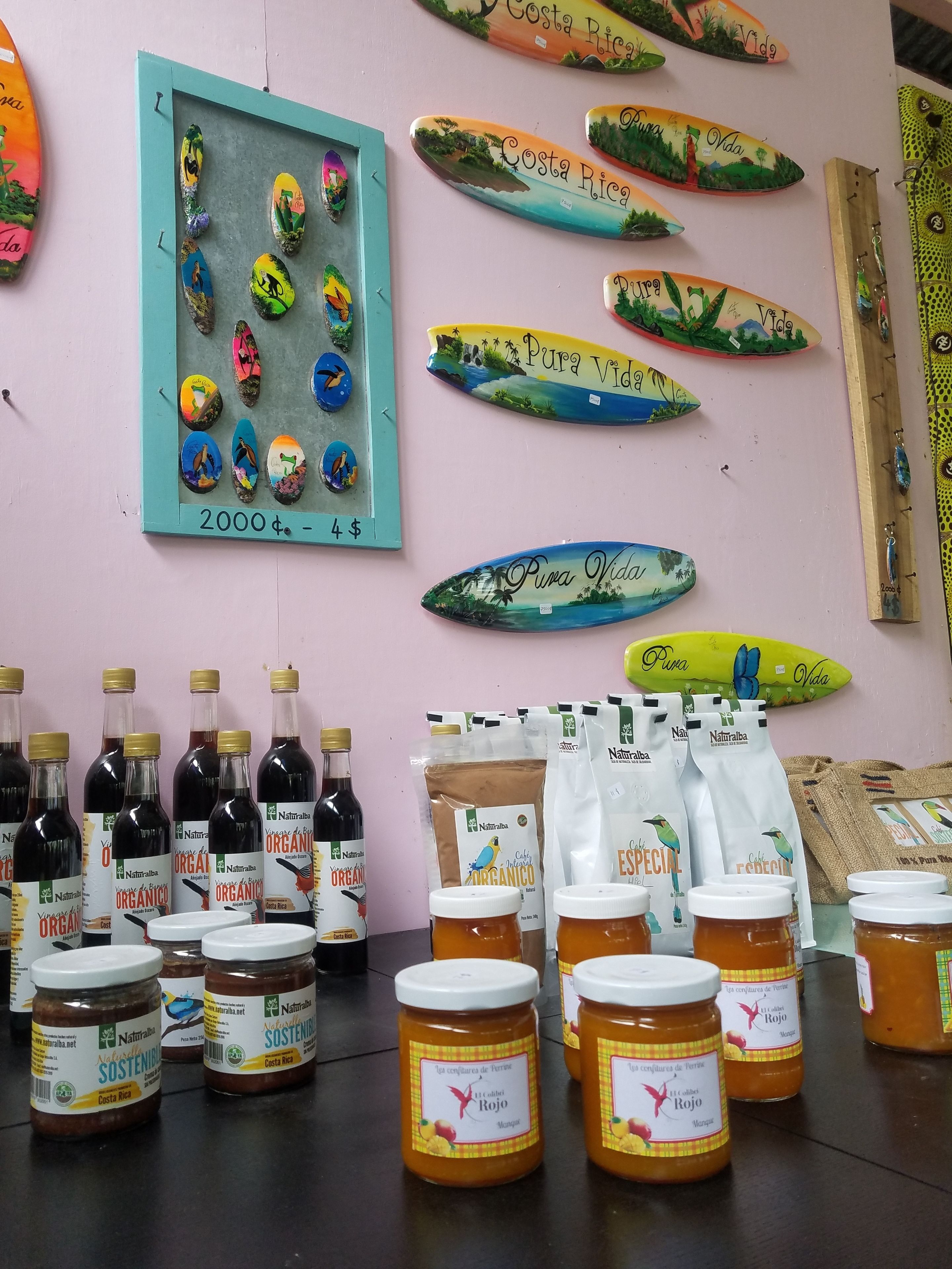 Exposició de records de Costa Rica, incloent aules de surf pintades, ampolles de productes orgànics costarenys i pots de melmelada de mango.