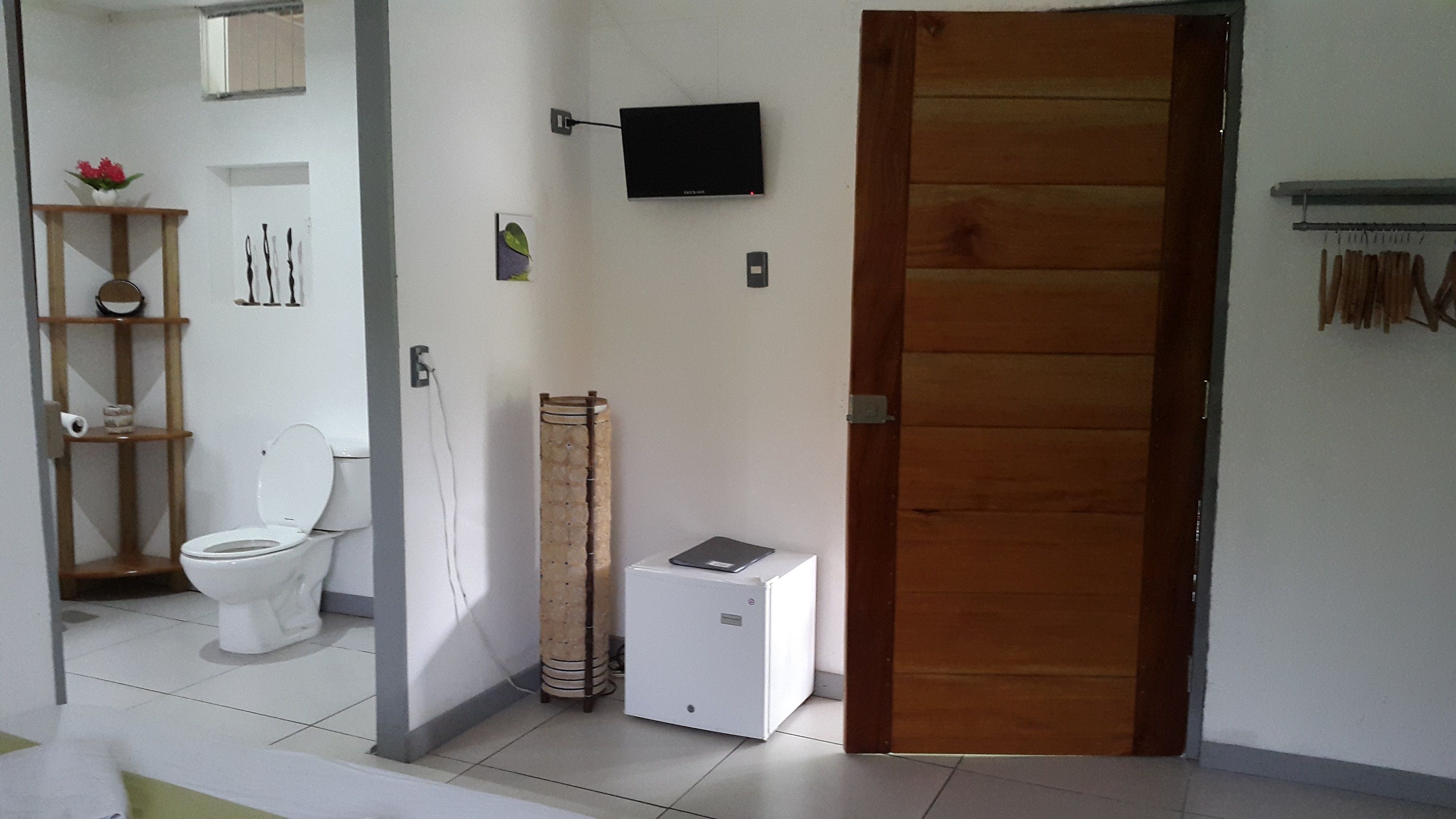 A bathroom with a toilet, a wooden door, a small white cabinet, and a wall-mounted TV.