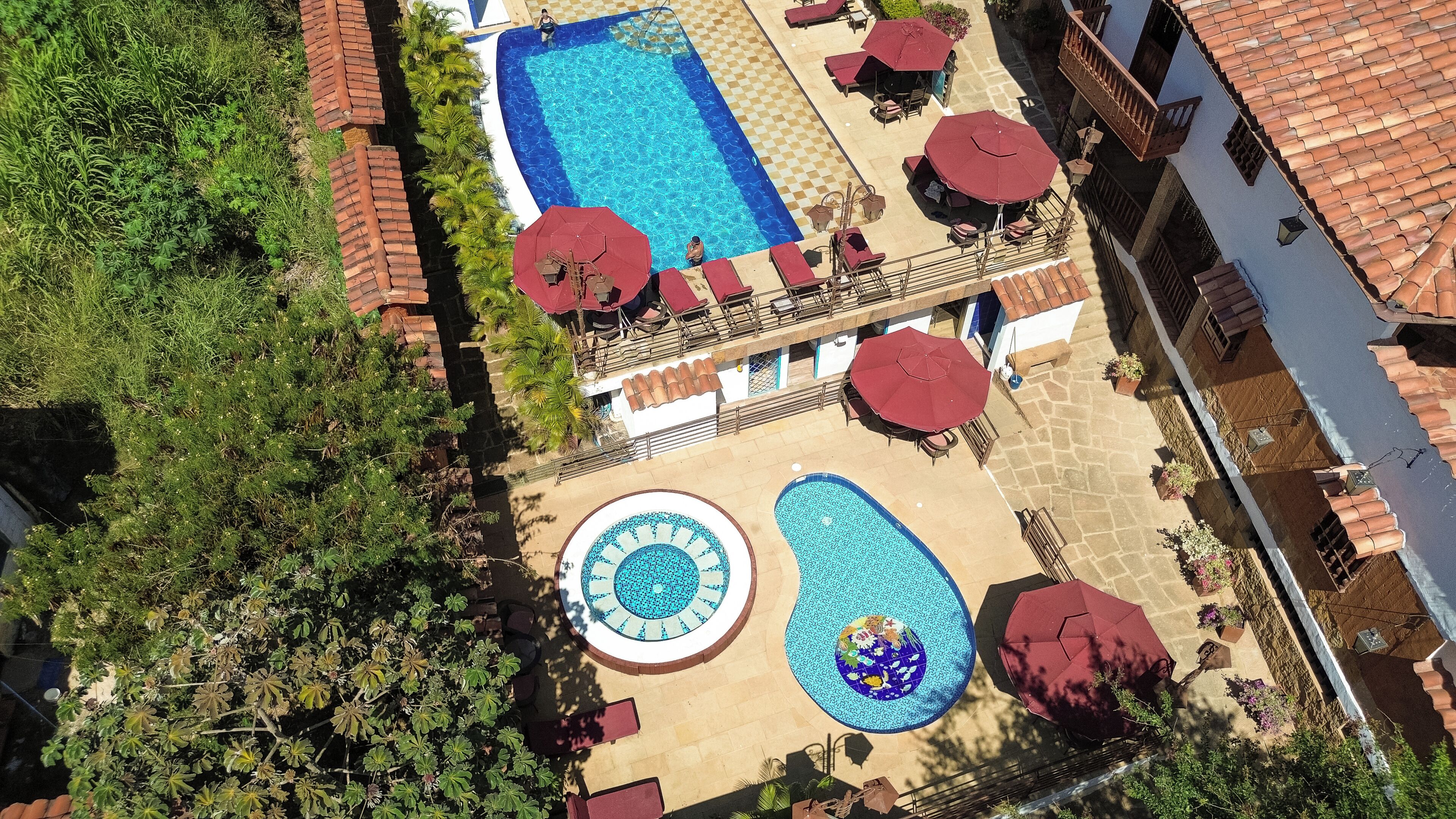 An aerial view of a hotel with a swimming pool, sun loungers, and a small circular pool.