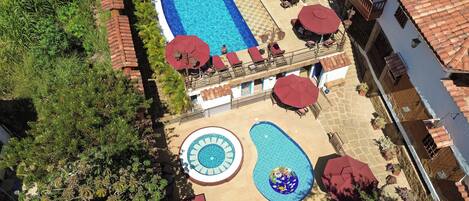 An aerial view of a hotel with a swimming pool, sun loungers, and a small circular pool.