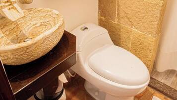 Un baño con pared de piedra, un lavabo redondo, un inodoro y un cubo de basura.