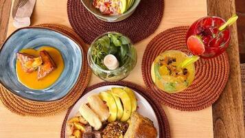 Una mesa de madera con varios platos, incluyendo un plato de carne y verduras, un bol de fruta y un vaso de bebida.