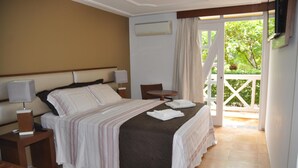 Une chambre d’hôtel avec un lit, une table de chevet avec une lampe, une chaise et une vue sur la verdure par une porte.