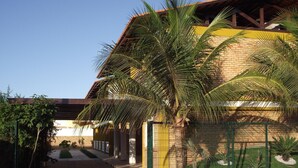 Un bâtiment à la façade en briques, doté d’un patio couvert et d’un jardin clos agrémenté de palmiers.