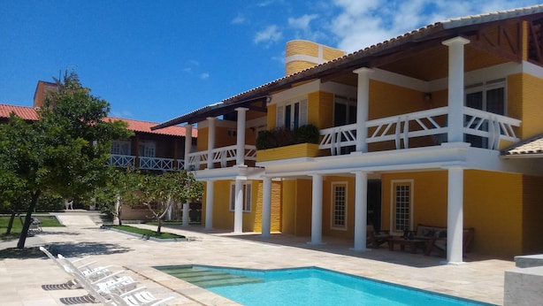 Un bâtiment jaune à deux étages, doté d’une piscine, de colonnes blanches et d’un patio couvert.