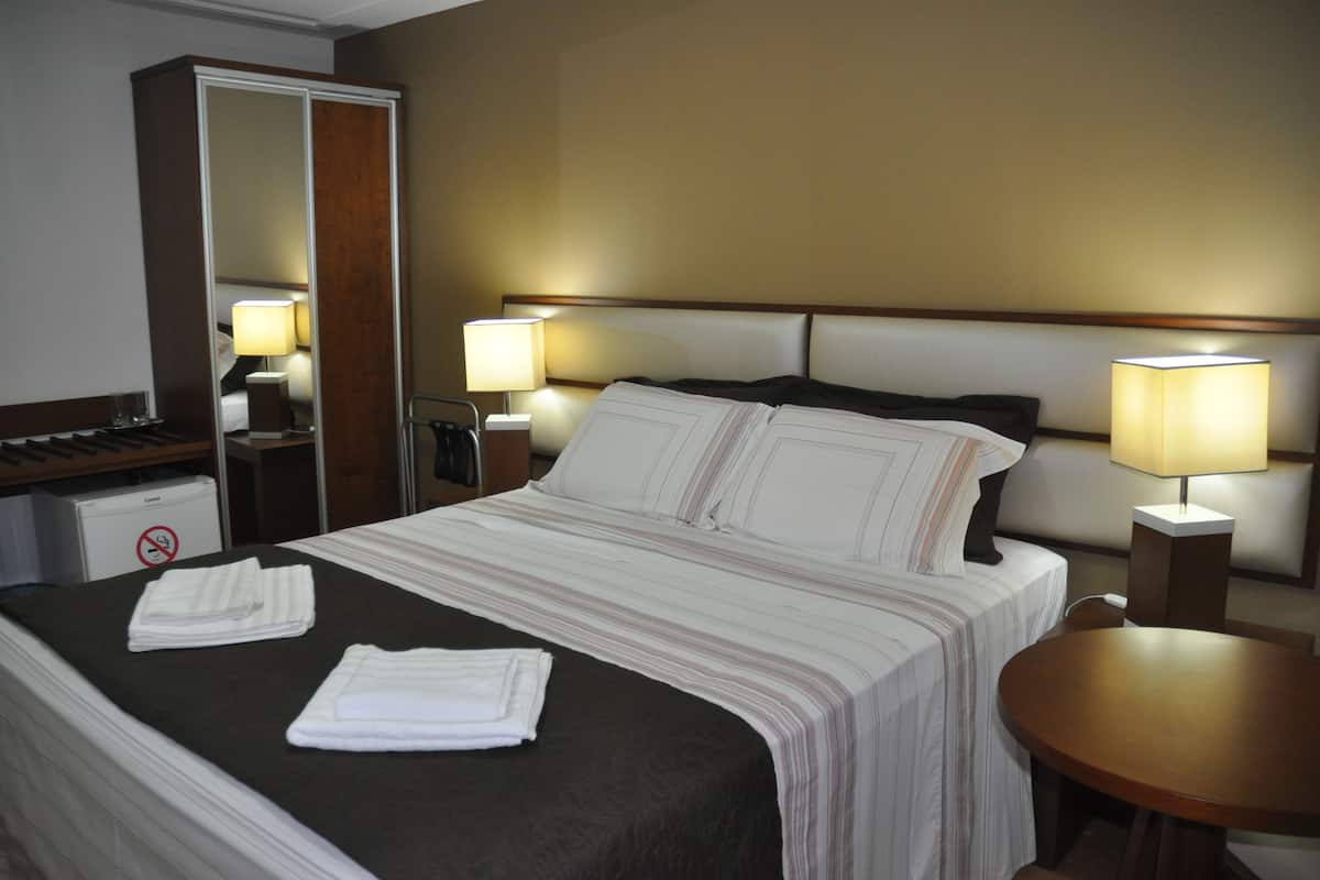 A hotel room with a large bed, two bedside lamps, a wooden nightstand, a round table, and a mirror with a wardrobe.