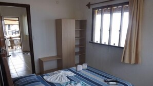 A hotel room with a bed, a wardrobe, a window with curtains, and a view of the dining area. - Pousada Restinga (Lauro de Freitas)