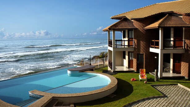 A beachfront hotel with a pool, a view of the ocean, and a two-story building with balconies. - Pousada Restinga (Lauro de Freitas)
