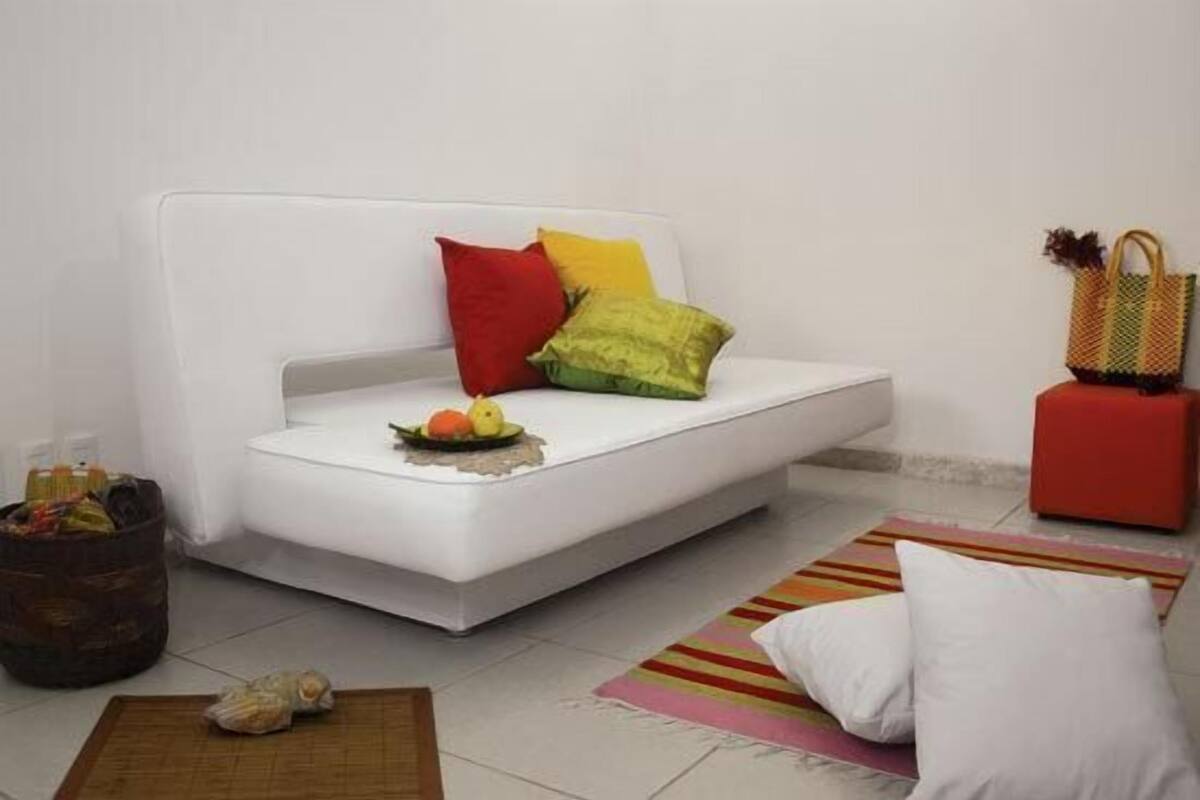 Ein modernes Wohnzimmer mit einem weißen Sofa, bunten Kissen, einer Obstschale und einem kleinen Tisch.