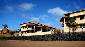 A coastal property with a stone wall, two-story buildings, and a clear blue sky. - Pousada Restinga (Lauro de Freitas)