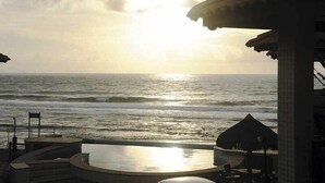 A beach view with a sunlit ocean, a thatched umbrella, and a pool area. - Pousada Restinga (Lauro de Freitas)