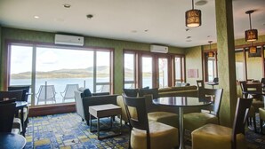 Comedor con vistas a un lago, con mesas y sillas redondas, piso estampado y ventanas amplias.