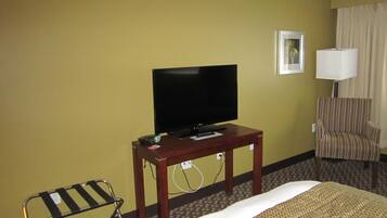 Habitación de hotel con una cama, un televisor sobre una mesa de madera, un sillón a rayas y una pequeña silla.
