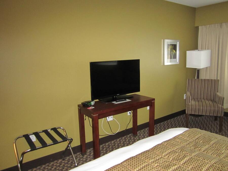 Habitación de hotel con una cama, un televisor sobre una mesa de madera, un sillón a rayas y una pequeña silla.