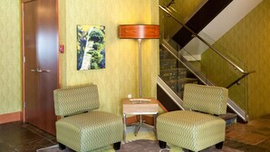Un vestíbulo con dos sillones estampados, una lámpara de pie, una mesita y una escalera.