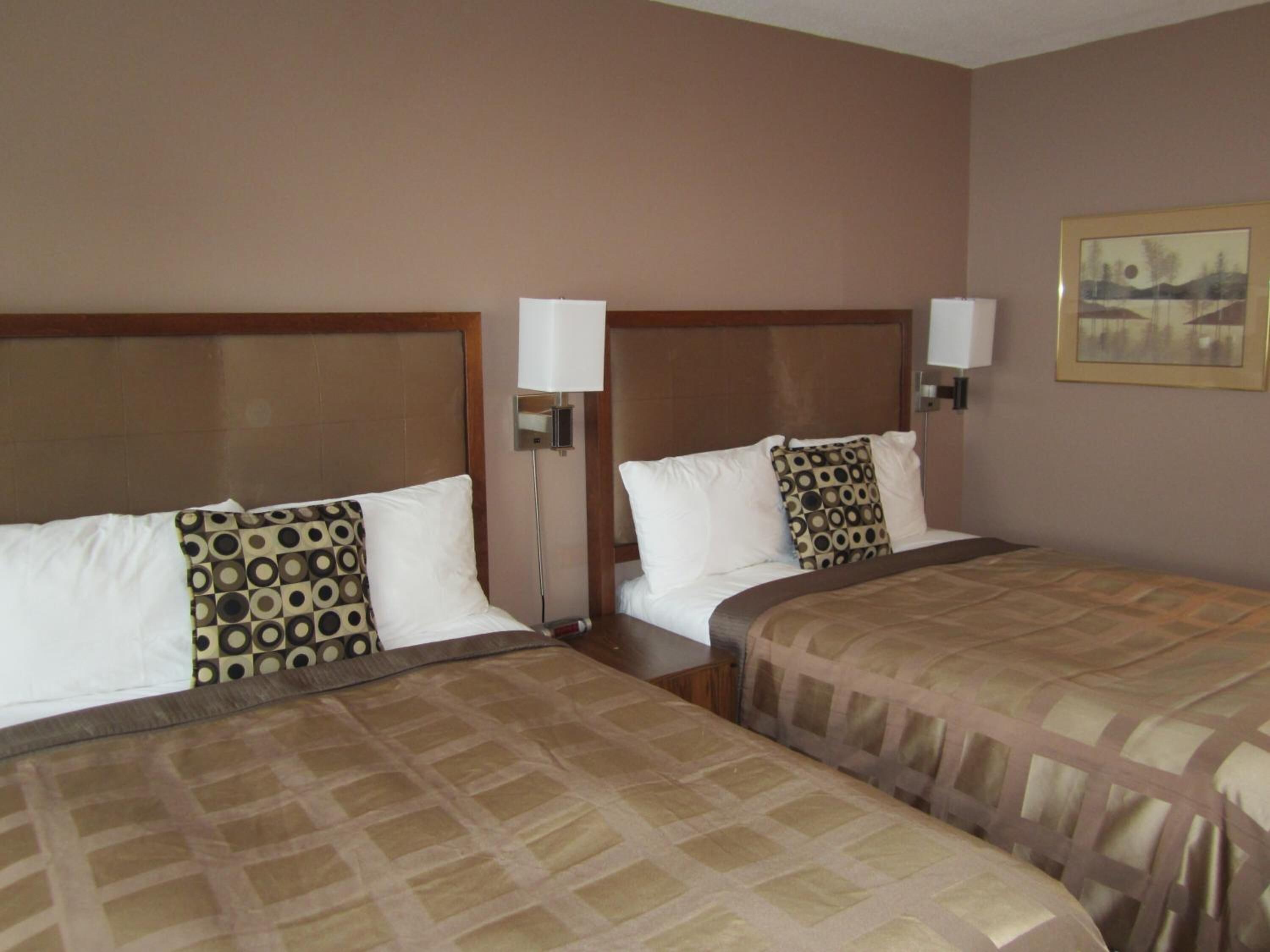 A hotel room with two beds, each with a patterned bedspread and matching pillows. There is a nightstand with a lamp between the beds.