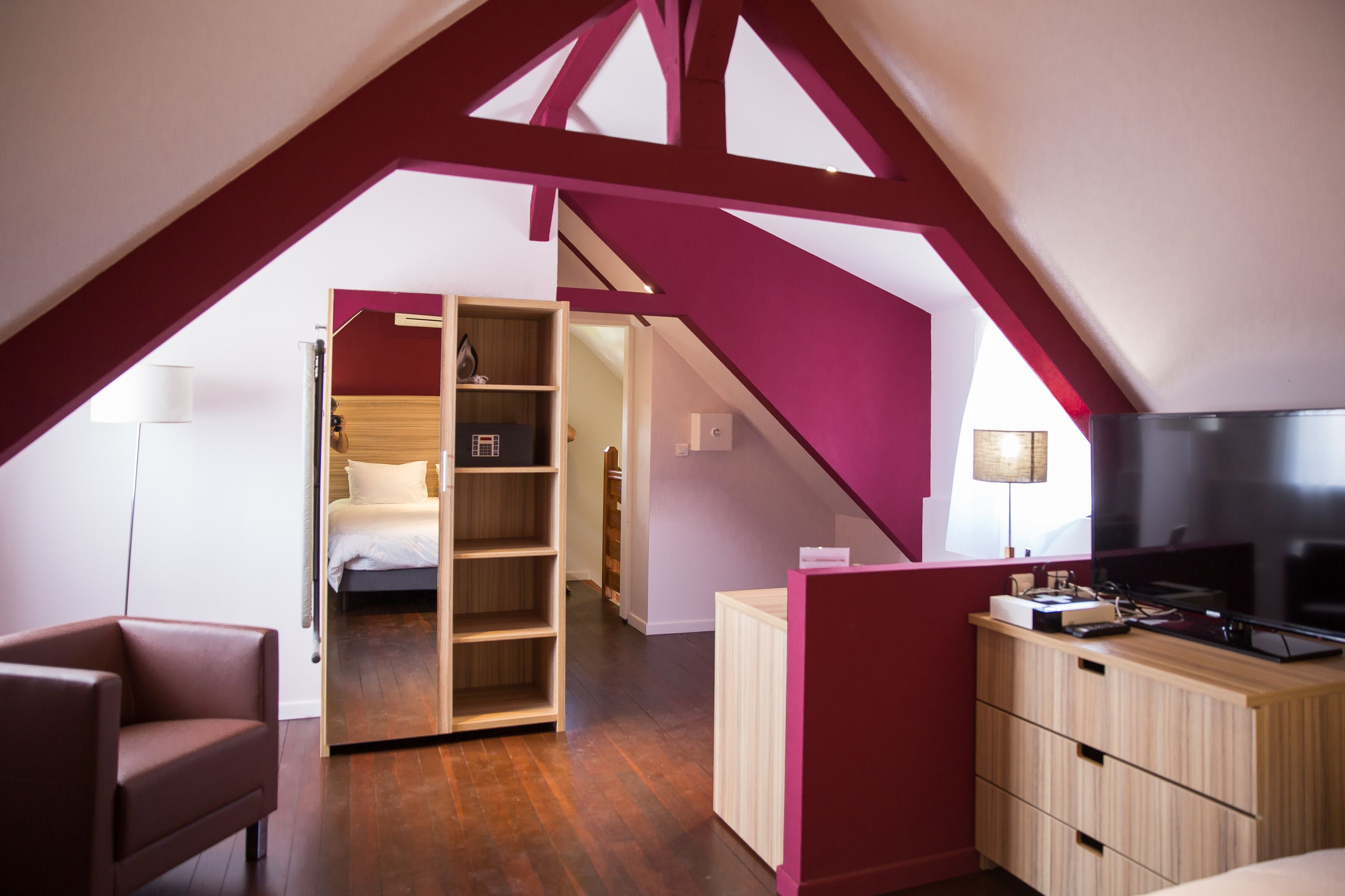 A modern loft bedroom with a sloped ceiling, wooden furniture, and a television.
