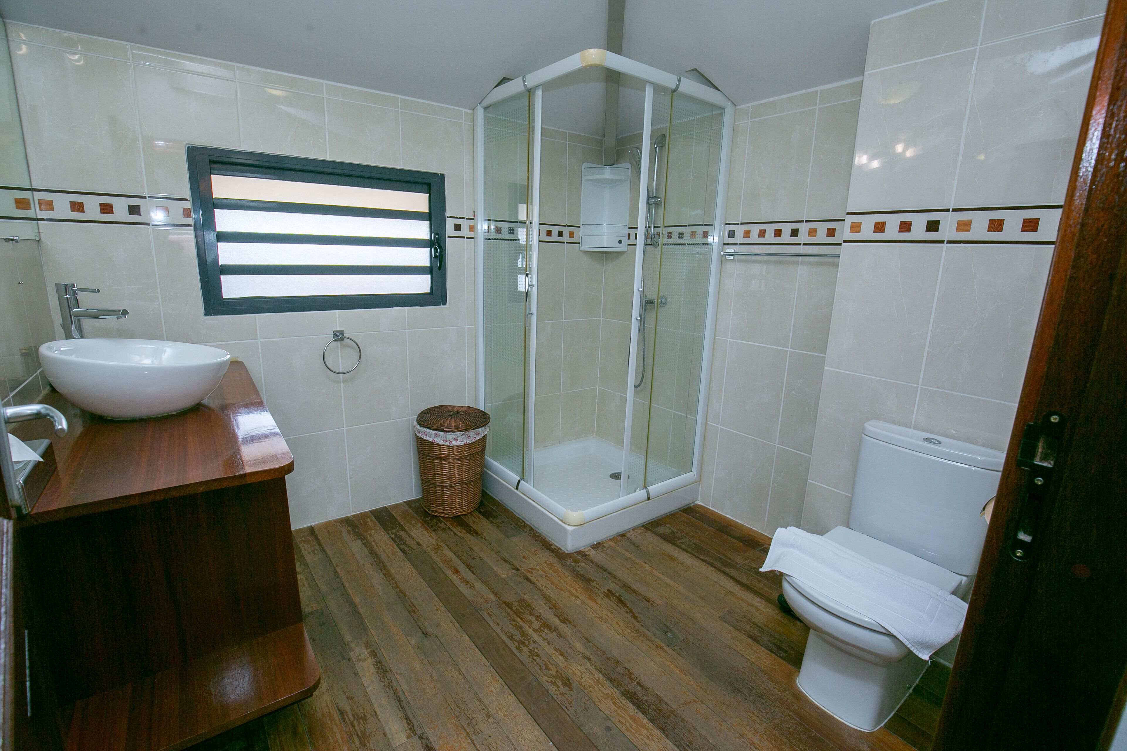 A bathroom with a wooden vanity, a white sink, a glass-enclosed shower, and a toilet.