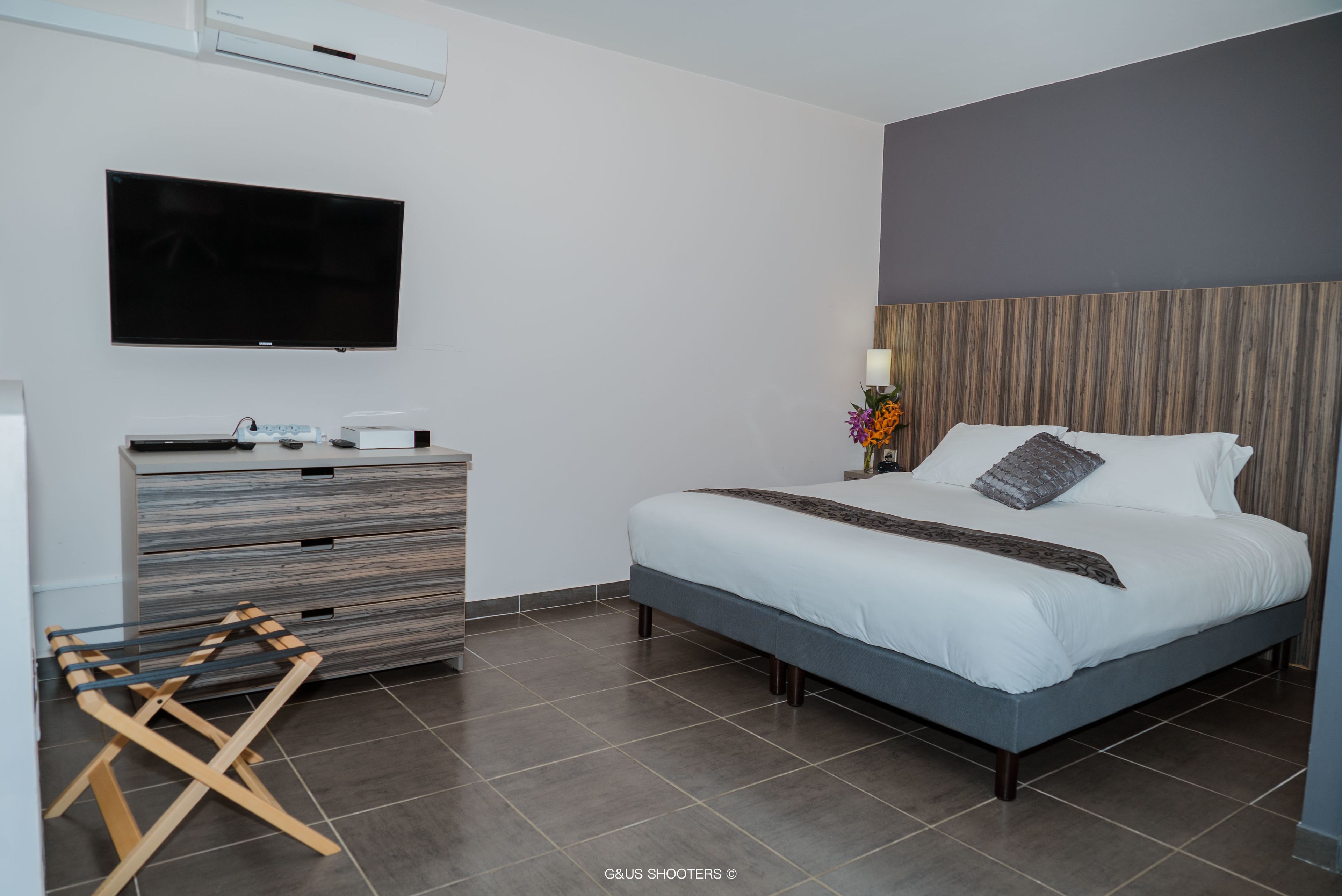 Un dormitorio moderno con una cama grande, un televisor de pantalla plana, un aparador de madera y un aire acondicionado de pared.