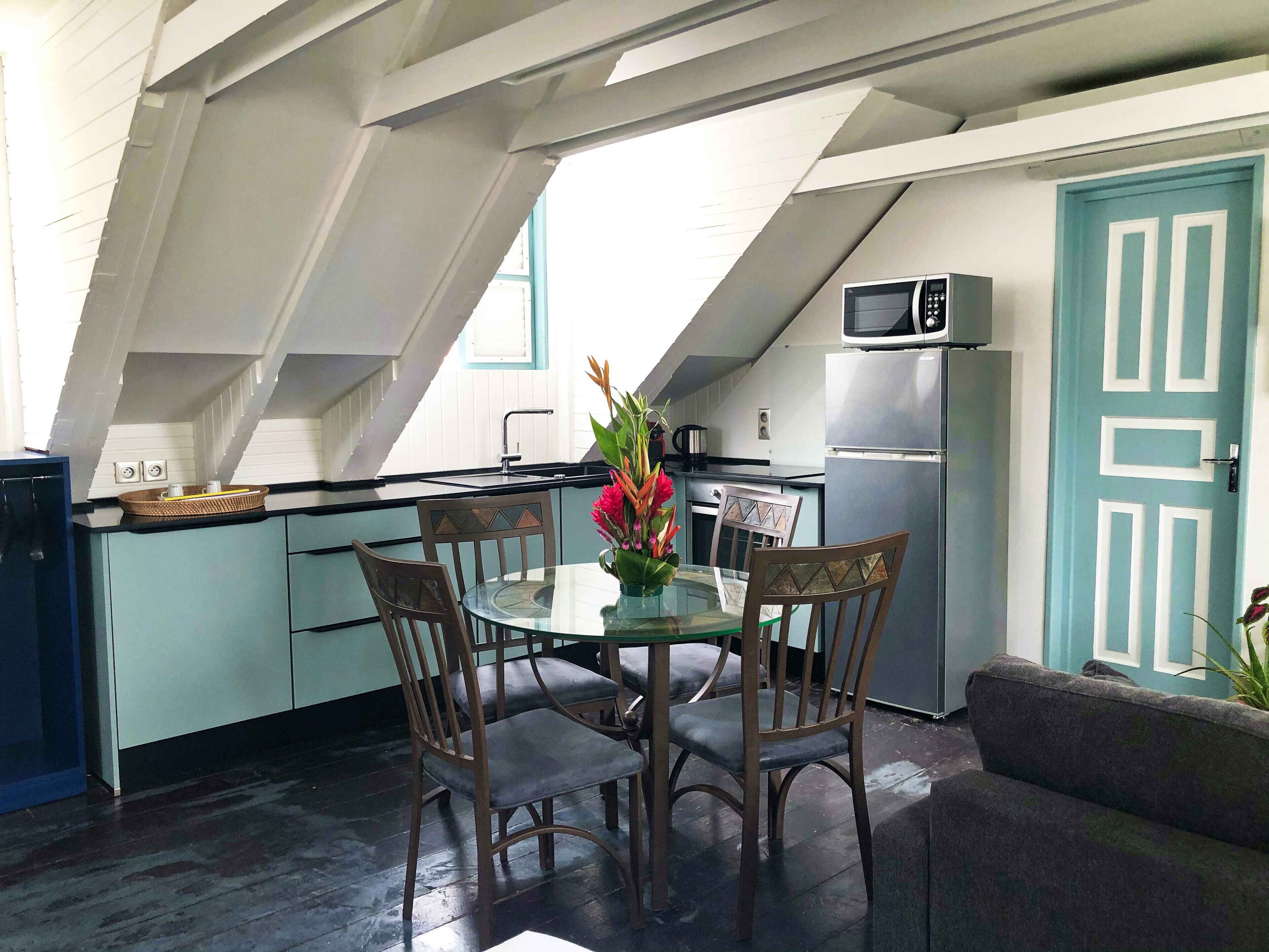 A modern kitchen with a dining area, featuring a glass table, wooden chairs, and a teal door.