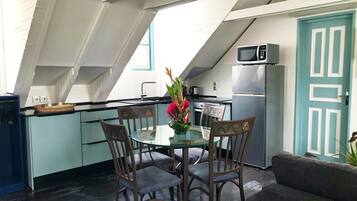 A modern kitchen with a dining area, featuring a glass table, wooden chairs, and a teal door.