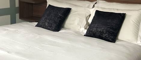 A neatly made bed with white bedding and two dark pillows.