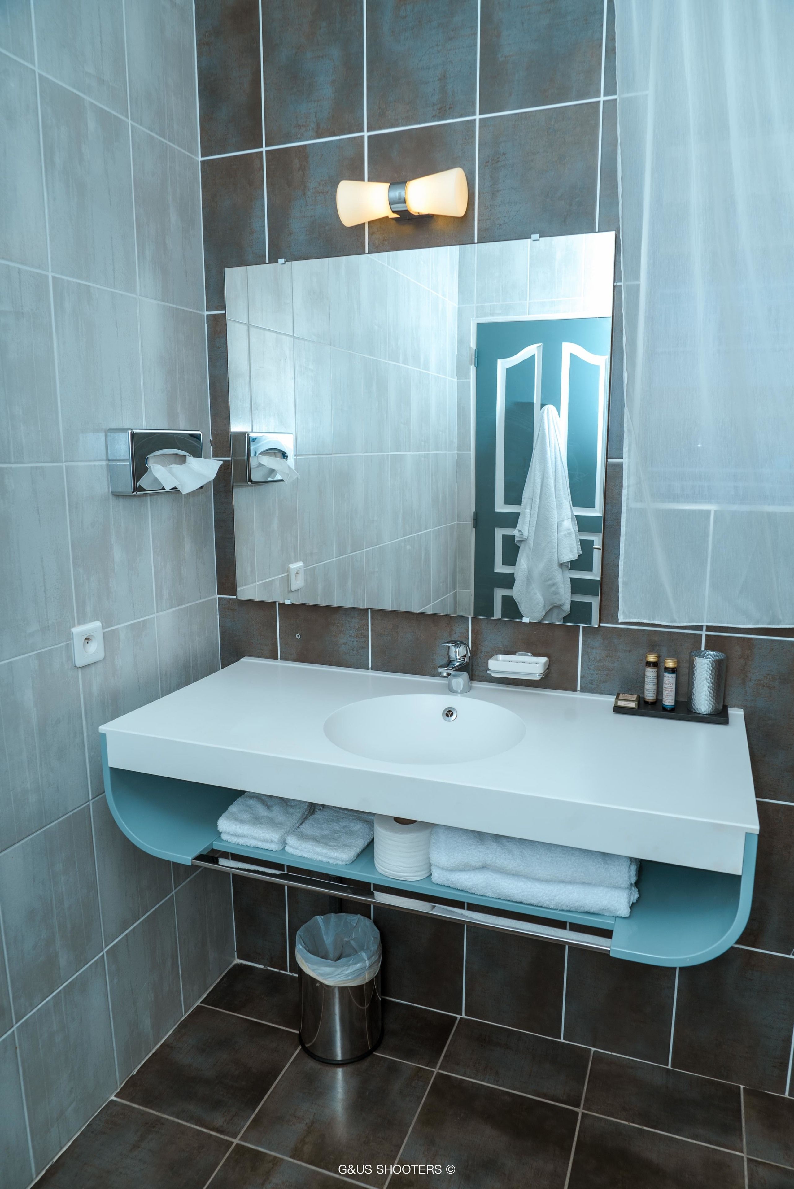 A modern bathroom with a white sink, a mirror, a towel rack, and a trash can.