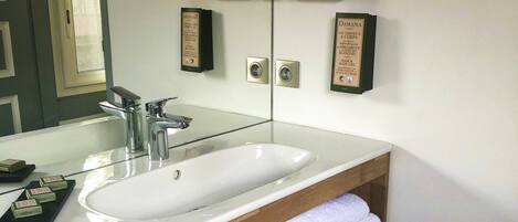 Un baño moderno con un espejo grande, un lavabo blanco y repisas de madera con toallas.