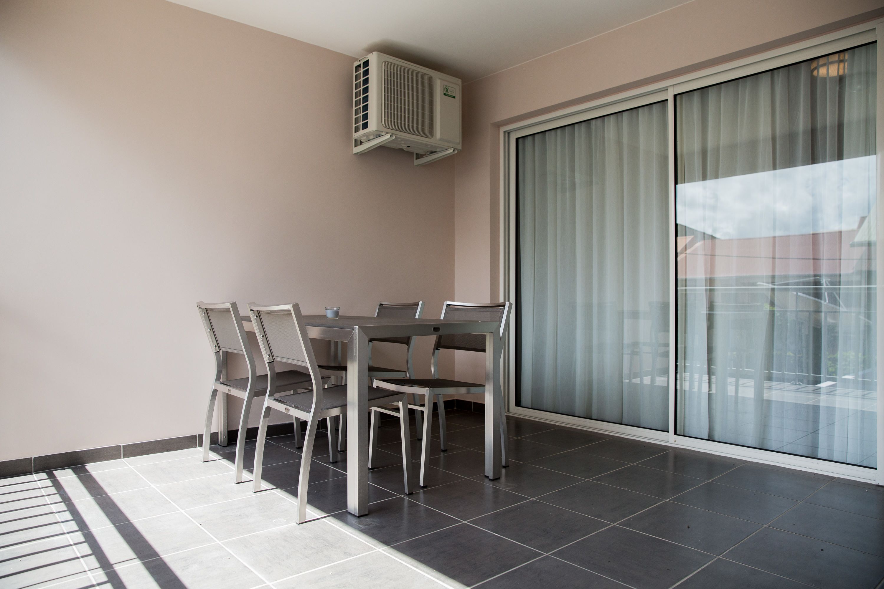 A balcony with a dining table and chairs, a sliding glass door, and an air conditioning unit.