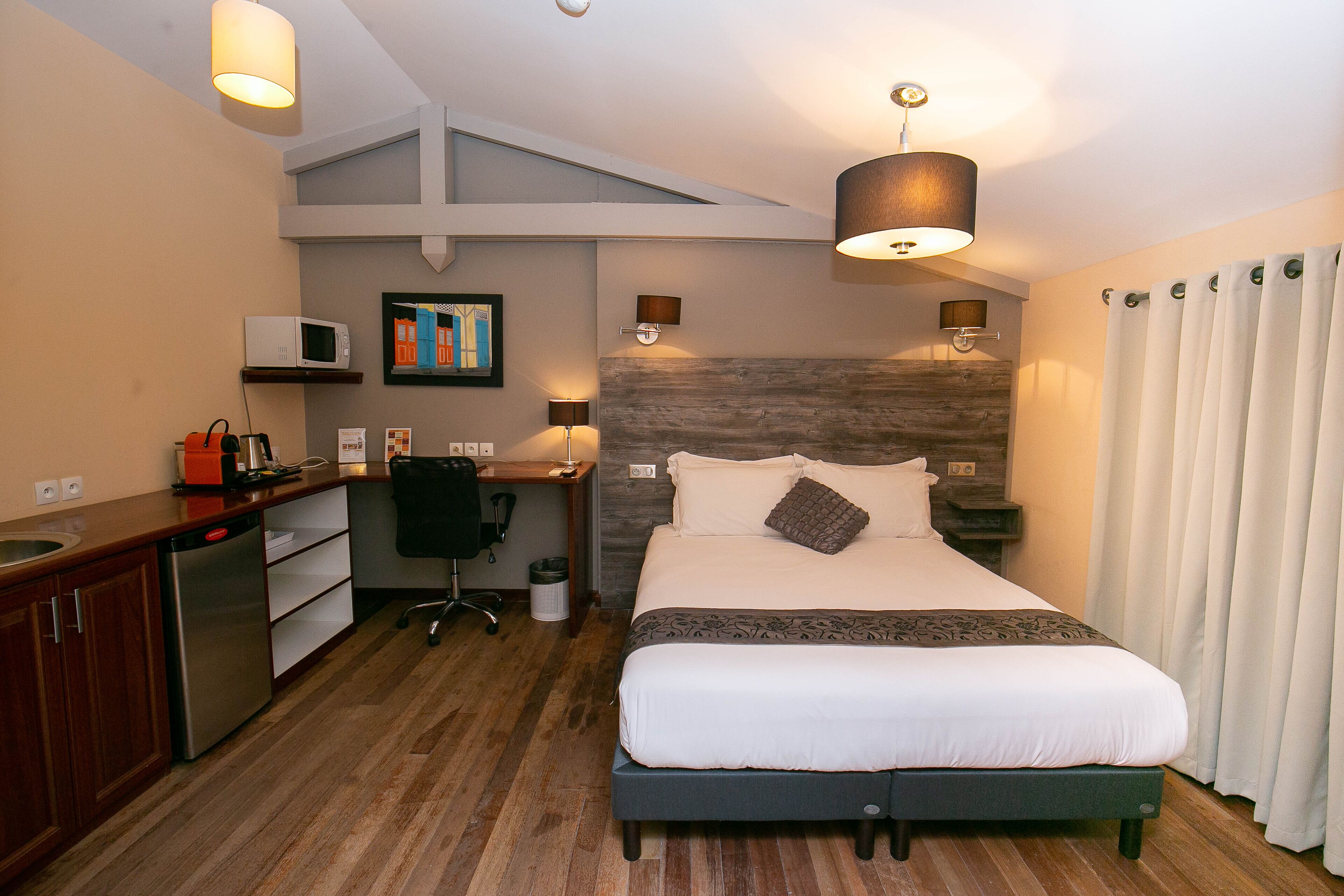 A hotel room with a bed, desk, and kitchenette.