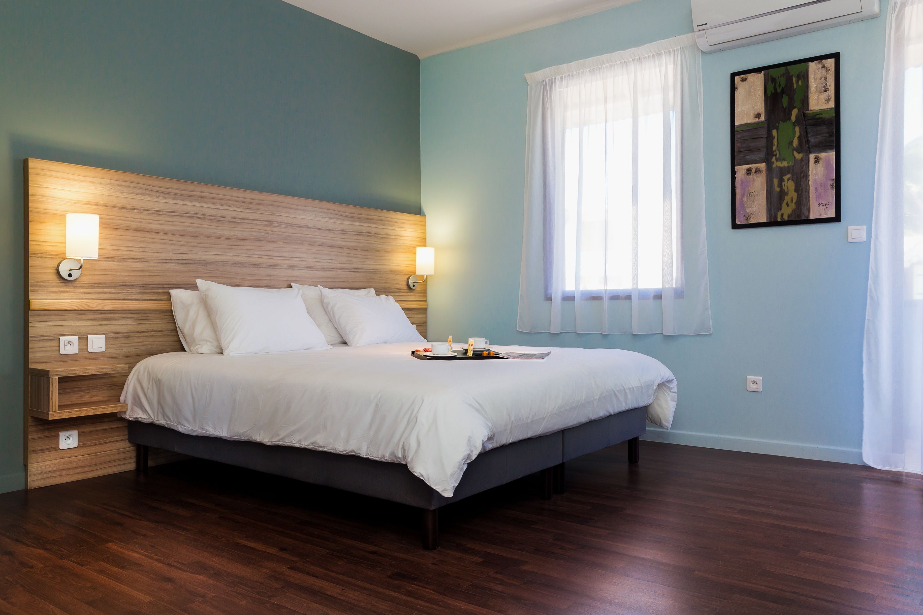 Una cama bien hecha con sábanas blancas, cabecera de madera y lámparas de noche.