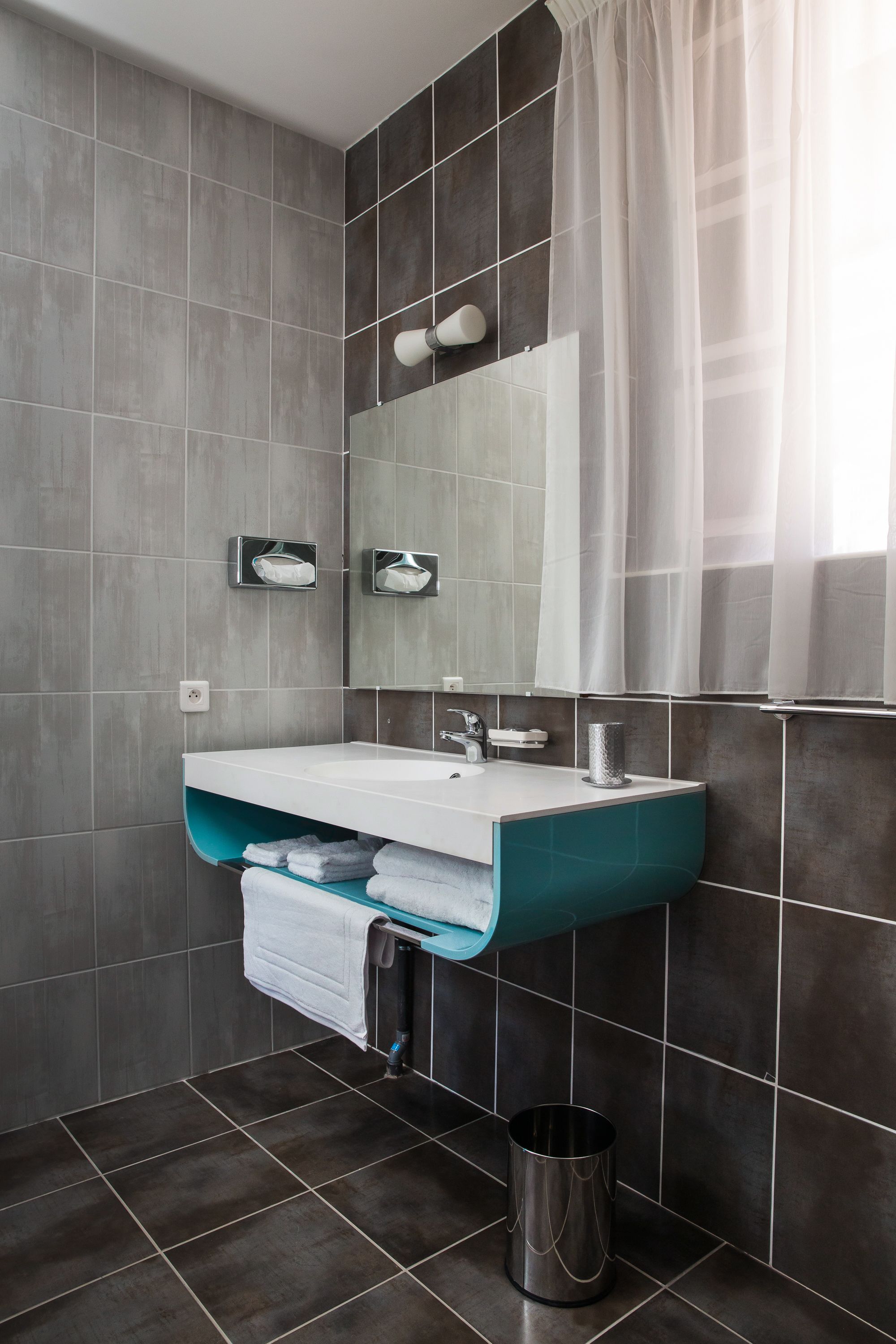 Une salle de bain moderne avec un lavabo blanc, des carreaux foncés, un miroir et un rideau de douche.