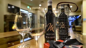 A bottle of Hotel Maison wine, a wine glass, and a gift box on a wooden table in a hotel setting.
