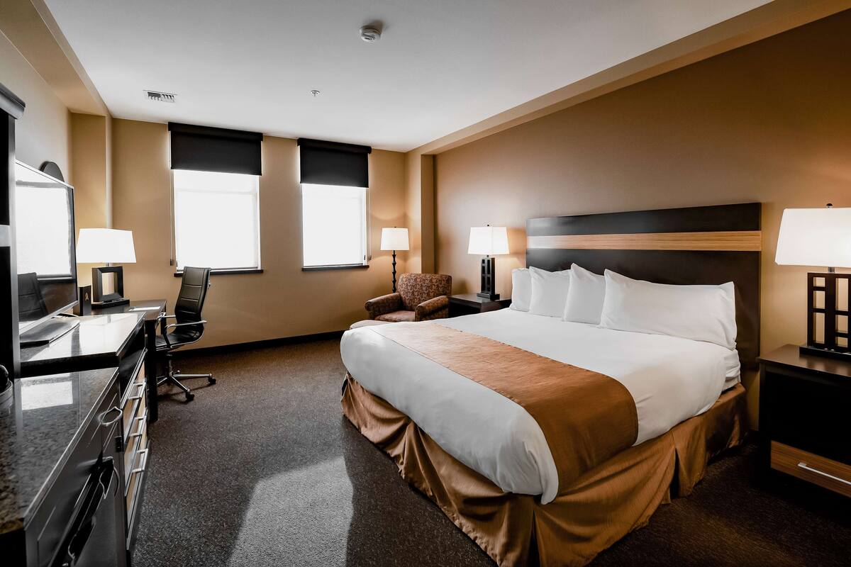 Une chambre d’hôtel avec un grand lit, deux tables de chevet avec des lampes, un bureau avec une chaise et un téléviseur.